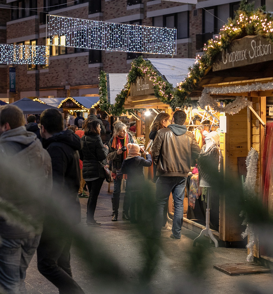 Un couple et des personnes devant un chalet dans un marché de Noël à Louvain-la-Neuve