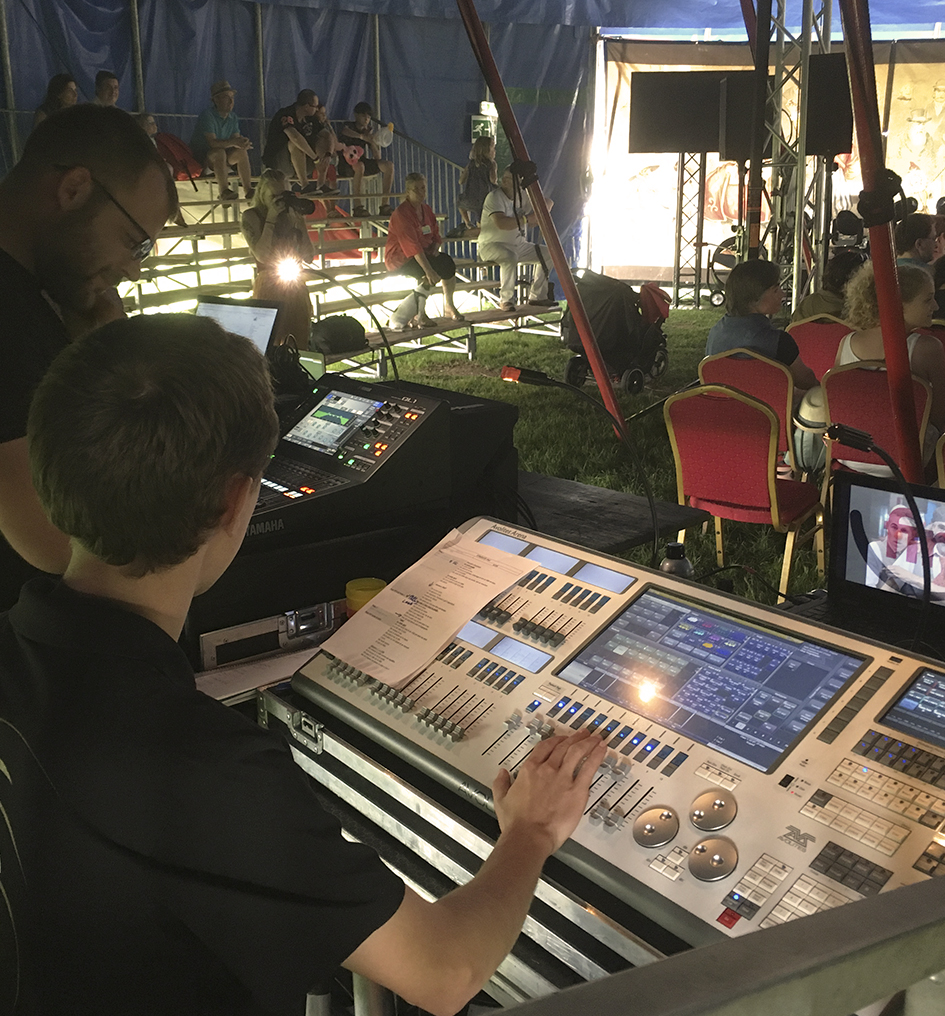 Deux régisseurs derrière une console et des écrans sous un chapiteau